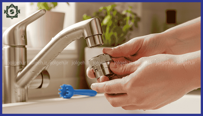 دست‌های شخصی در حال باز کردن یا تمیز کردن پرلاتور (سرشیر) یک شیر آب آشپزخانه استیل.